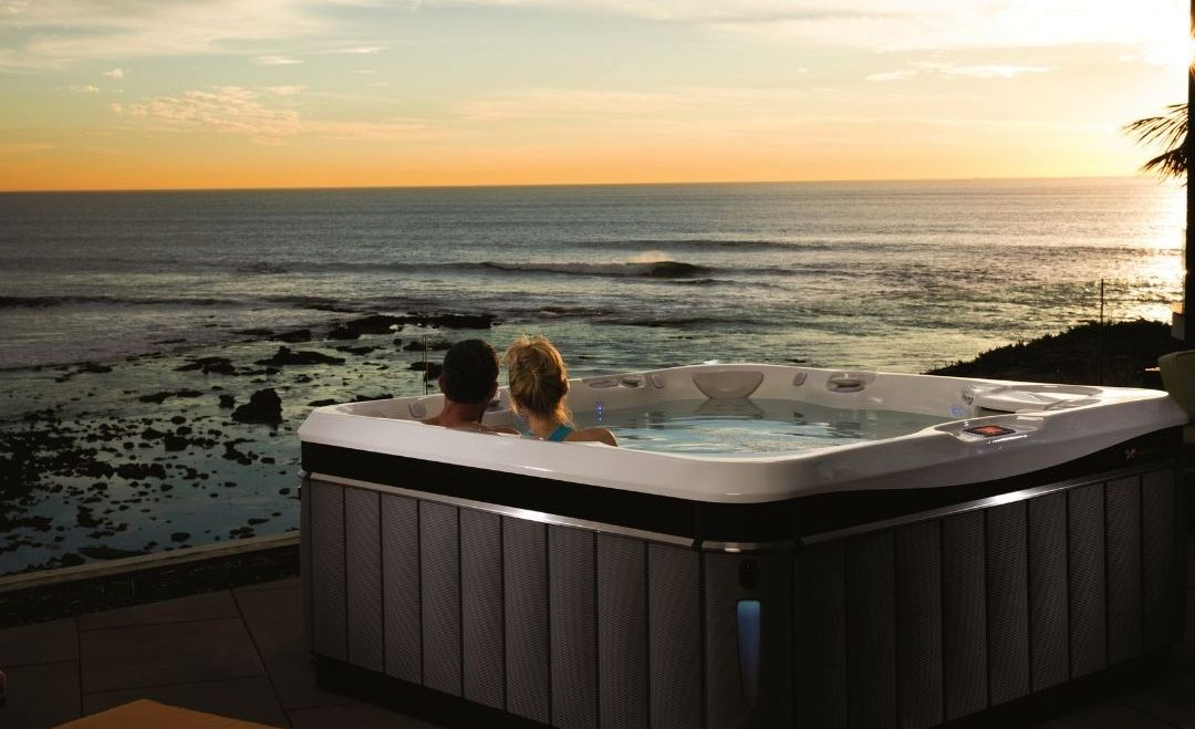 Couple in a hot tub overlooking the ocean at sunset